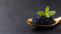 Fresh black caviar served on wooden spoon with mint leaf garnish against dark background, luxury gourmet appetizer for fine dining and celebrations.