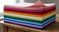 Stack of colorful felt fabric sheets arranged in rainbow spectrum on wooden surface. Craft materials for sewing, DIY projects and textile arts.