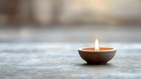 Small clay oil lamp with glowing flame on wooden surface creating warm ambient lighting for meditation, spirituality and relaxation concepts.
