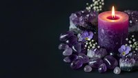 Burning pink candle surrounded by purple amethyst crystals and white flowers on dark background for meditation, spa treatments and spiritual healing rituals.