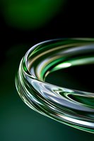 Abstract curved metallic surface with green and silver reflective waves creating dynamic motion effect against dark background.