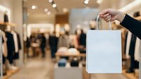 Customer holding white shopping bag in modern retail clothing store with blurred background, representing retail commerce and consumer shopping experience.