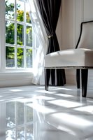 Elegant white armchair near window with black curtains on glossy marble floor, sunlight casting shadows through windowpanes in luxurious bright interior.