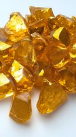 Amber colored crystal fragments with translucent geometric shapes catching light and creating golden reflections on white background, suitable for jewelry design concepts.