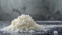 White coarse sea salt crystals pile on dark surface with scattered grains around for cooking and seasoning culinary applications.