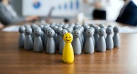 Yellow wooden pawn stands out among gray pawns on office desk, symbolizing leadership, uniqueness and standing out from crowd in business environment.