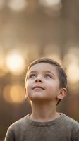 Young boy looking up with wonder and curiosity against warm golden bokeh background during golden hour light for childhood and inspiration concepts.