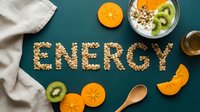 Word ENERGY spelled with granola oats on dark teal background, surrounded by fresh kiwi, persimmon, yogurt bowl, honey, and wooden spoon.