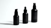 Black cosmetic spray bottles in different sizes arranged on white background for skincare and beauty product packaging design.