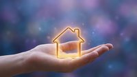 Glowing house icon floating above open palm against dreamy bokeh background symbolizing home protection, real estate investment and property dreams.