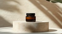 Amber glass cosmetic jar on beige stone podium with soft shadow overlay and minimal aesthetic styling for luxury skincare product photography.