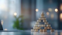 Wooden blocks arranged in pyramid shape on table with soft bokeh background, symbolizing business hierarchy, growth strategy, and organizational structure.