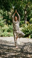Middle-aged Caucasian woman practicing tree pose yoga outdoors on stone patio surrounded by lush green garden foliage for wellness and mindfulness.