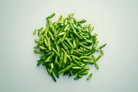 Fresh green chili peppers sliced lengthwise in pile on light background, raw spicy ingredient for Asian cuisine and hot dishes.