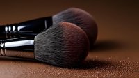 Professional makeup brushes with soft black bristles and powder particles on brown background, close-up macro shot showing texture and detail for cosmetic and beauty industry.