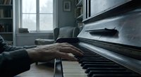 Hands of mature musician playing piano keys in cozy home interior with natural window light creating peaceful atmosphere for music practice and relaxation.