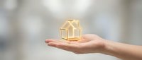 Golden house model floating above open palm symbolizing real estate investment, property protection, home insurance and mortgage lending services.