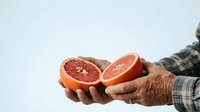 Mature man with wrinkled hands holding fresh grapefruit halves, displaying juicy citrus fruit for healthy eating, nutrition, and organic produce concepts.