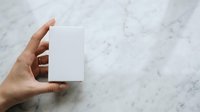 Close-up of hand holding blank white card on marble surface for branding, stationery mockup, and business card design presentations.