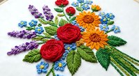Colorful hand embroidered floral bouquet with roses, sunflowers and lavender on white fabric in embroidery hoop for needlework and craft projects.