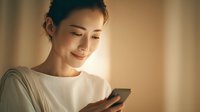 Young Asian woman smiling while using smartphone in warm indoor lighting. Modern lifestyle technology communication concept for social media marketing.