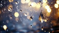 Raindrops on glass window with golden bokeh lights creating magical atmosphere. Water droplets reflect warm evening glow against dark blue background.