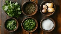 Fresh cooking ingredients in wooden bowls on rustic dark table including parsley, dried herbs, garlic, chopped herbs and sea salt arranged in culinary composition.