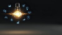 Glowing light bulb with business icons and charts floating around representing innovation, creativity, and entrepreneurial ideas on dark background.