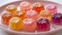 Colorful translucent jelly candies with floral patterns arranged on pink plate. Sweet gummy treats in rainbow colors for dessert and confectionery concepts.