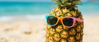 Tropical pineapple wearing colorful sunglasses on sandy beach with turquoise ocean background, summer vacation and holiday concept for travel marketing.