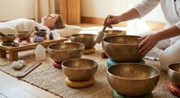 Sound healing therapy session with Tibetan singing bowls and relaxed woman receiving holistic wellness treatment in spa setting.