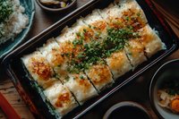 Grilled rice rolls topped with melted cheese, green onions and spicy seasoning served in traditional Asian black rectangular plate with side dishes.