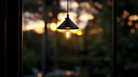Glowing vintage pendant lamp with edison bulb against blurred sunset background creates cozy atmospheric lighting and warm bokeh effect at dusk.