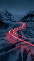 Glowing red light trails curve through a snow-covered mountain valley at dusk, creating a striking contrast against the frozen landscape and dark peaks. Long exposure photography.