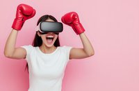 Excited Asian woman wearing VR headset and red boxing gloves celebrating victory on pink background. Virtual reality gaming and fitness technology concept.