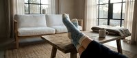 Cozy home relaxation scene with feet in warm knitted socks resting on a rustic wooden coffee table in a bright Scandinavian living room.