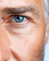 Close-up macro shot of mature Caucasian male blue eye with wrinkles and skin texture details, showing natural aging process and wisdom in facial features.