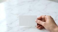 Hand holding blank white business card against marble surface for branding and corporate identity mockup presentations.