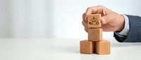 Businessman hand placing wooden cube with crown symbol on stack representing leadership hierarchy and corporate success in office environment.