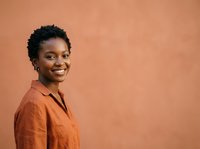 Smiling African American woman with short curly hair wearing rust-colored linen shirt against warm terracotta background, suitable for corporate portraits and professional headshots.