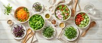 Assorted fresh salad bowls with greens, vegetables, and microgreens on a white wooden table with wooden utensils, healthy eating concept.