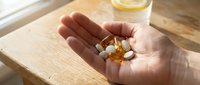 Caucasian hand holding dietary supplements and vitamins on wooden surface with water glass, wellness and health concept for nutritional products and healthcare marketing.