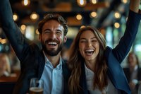 Young diverse business colleagues celebrating success with arms raised, expressing joy and achievement in modern office with bokeh lights. Authentic workplace emotion.