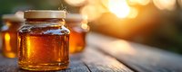 Glass jar filled with golden honey glowing in warm sunset light on rustic wooden table, with additional honey jars creating bokeh effect in background.