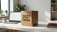 Wooden cube displaying 2027 TRENDS text on modern office desk with laptop, plants and books in bright workspace for business planning and forecasting.