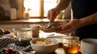 Man preparing healthy breakfast with chia seeds, nuts and honey in warm sunlit kitchen. Nutritious morning meal preparation concept.