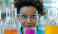 African American female scientist in laboratory examining colorful liquid samples in glass beakers. Close up portrait showing protective eyewear and professional expertise.