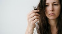 Young woman examining damaged hair split ends with concerned expression, hair care and treatment concept for beauty and wellness industry.