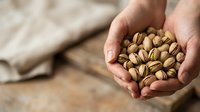 Hands holding roasted pistachios with shells, displaying fresh nuts for food, nutrition, snacking, cooking ingredients, and healthy eating concepts.