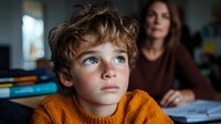 Young boy with curly hair and blue eyes wearing orange sweater gazes upward thoughtfully while woman sits in background during homework or study session.